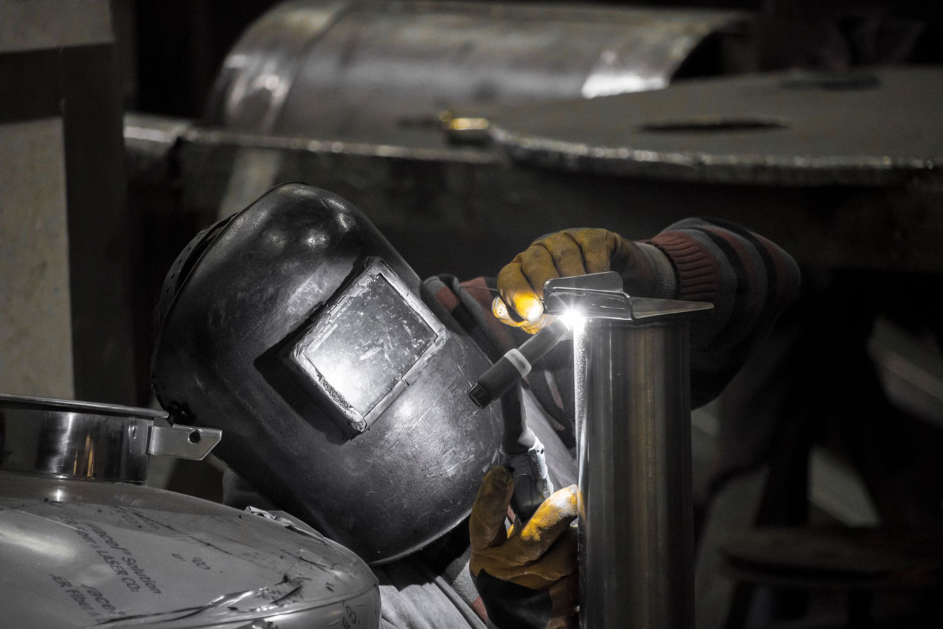 A welder working on a stainless steel assembly